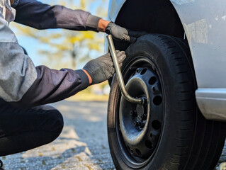 Fototapeta premium A man fastening or loosening wheel nuts during seasonal tire replacement. Symbol of car repair, safety check and mobility.