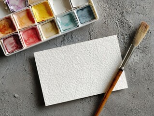 Watercolor Palette, Brush, and Paper on Textured Surface