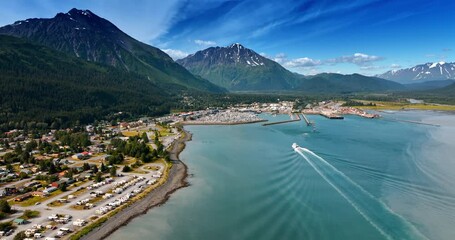 Urban area at the waterfront of the beautiful turquoise lake in the mountains. A boat moves by the waterscape to the shore. Alaska, USA.