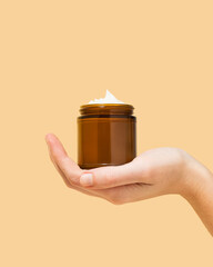 Woman holding amber glass jar of beef tallow moisturizer on pastel yellow background 
