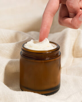 Woman's finger reaching for whipped beef tallow moisturizer in amber glass jar