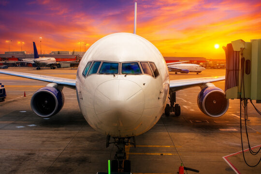  AI-Generated image of a commercial airplane at an airport gate during a vibrant sunset.