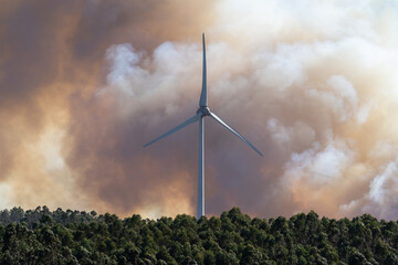A dramatic wildfire burns near a windmill under a sky filled with thick clouds. The contrast between renewable energy and destructive flames highlights themes of climate change, environmental crisis, 
