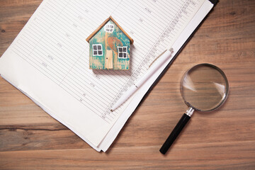 House model and magnifying glass on a notepad with pen on wooden background