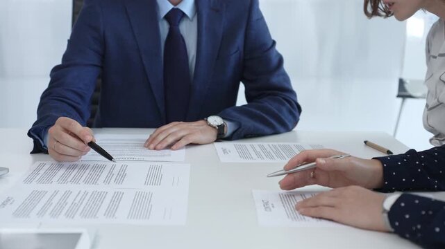 Business people analyzing contract details, gesturing with pens and hands while discussing legal terms during collaborative meeting, focused on negotiation process