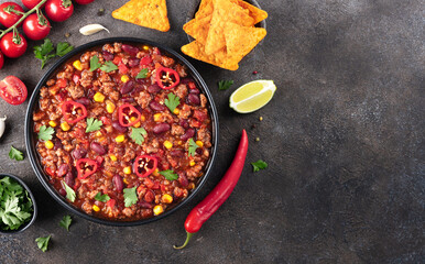 Chili con carne with fresh herbs and nachos chips on a gray background. Top view. Copy space. Mexican cuisine. 