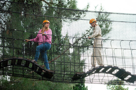 Adventure Park Couple Rope Bridge Two people in hard hats walk across a rope bridge at an outdoor adventure park.