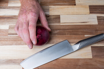 Hand cutting onion with kitchen knife on wooden board
