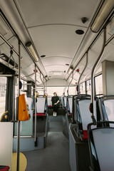 Wide-angle view of a stylish woman in sunglasses sitting alone at the back of a bright, empty city bus. Great for depicting urban commuting, independence, and quiet transport moments.