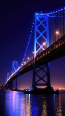 Obraz premium A magnificent suspension bridge, illuminated by vibrant blue lights, spans a calm body of water at night.