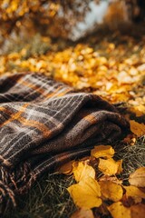 Folded tartan wool throw on grass amid golden fall leaves, warm outdoor close up