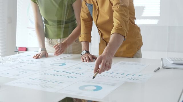 Business professionals analyzing financial reports, pointing at charts during collaborative meeting, discussing data with focused professional demeanor - Powered by Adobe