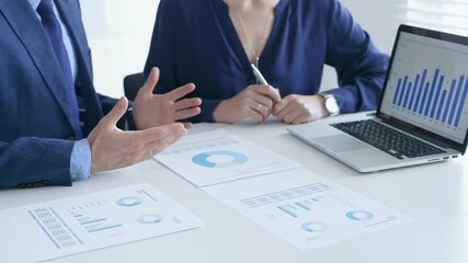 Business colleagues discussing financial data on a laptop and printed documents, analyzing charts and market trends for decisions. Business people and finance concept - Powered by Adobe