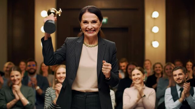 Mature woman holding award, receiving applause from audience, business success, achievement, presentation