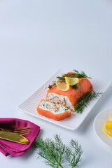A cold appetizer, a terrine of salted salmon and smoked mackerel with cheese cream and dill, served on a white rectangular plate against a white background.