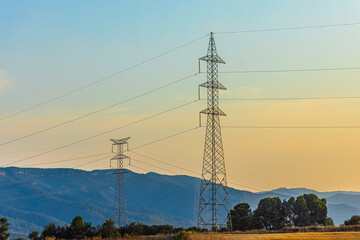 Silhouette of a black electricity transmission tower with power lines stretching across the sky at sunset