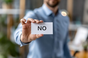 A Man Holding a Card Stating 'No' in a Bright, Modern Workspace, Expressing Disagreement or Refusal with Clear Communication