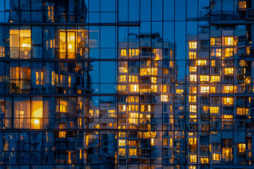 Reflection of illuminated apartment buildings on glass facade at dusk