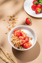 Granola or muesli with natural greek yogurt and strawberry in a bowl on a beige background with fresh berries