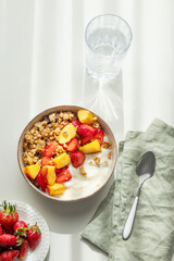 Granola or muesli with natural greek yogurt, strawberry and peach in a bowl on a white background