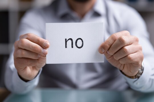 A Close-Up View of a Person Holding a Card with the Word 'No' Written in Bold to Emphasize a Clear Refusal or Negative Response in a Professional Setting