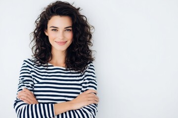 Obraz premium Cheerful young woman with curly hair wearing striped top smiling confidently indoors.