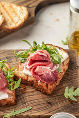 Grilled toasts with ham, cheese and arugula on wooden cutting board on light textured background close up. Delicious breakfast or snack