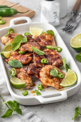 Spicy grilled chicken thighs roasted with chilli and lime on white dish, light gray kitchen background close up