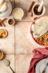 Freshly baked glazed cinnabon buns in ceramic baking dish, beige tile background. Making cinnamon rolls process with text space, top view