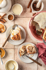 Freshly baked glazed cinnabon buns in ceramic plates, beige tile background. Cinnamon rolls serving, top view