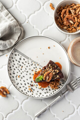Chocolate spongy brownie cake served with walnuts and mint on top and coffee on white tile background. A piece of chocolate brownie top view