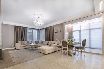 A modern living room with an elegant sofa, chandelier and dining area in a well-lit apartment.