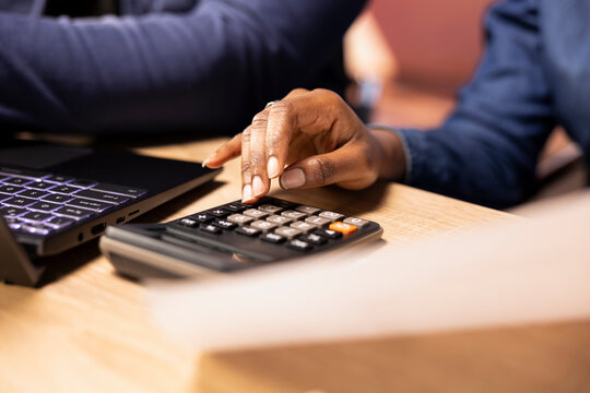 Black couple doing their taxes and accounting for a debt free tax season, using a calculator and laptop to track expenses and manage their bills. Financial responsibility. Close up.