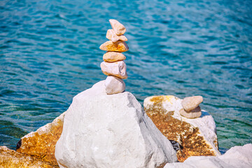Perfectly balanced stone cairn stands resiliently against tranquil blue sea, symbolizing peace and harmony. Serene image offers calming touch for any project seeking natural beauty and quiet strength