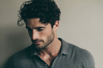 Obraz premium Close up of a thoughtful young man with dark curly hair looking downward indoors.