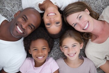 Obraz premium Happy multicultural family lying together on carpet smiling indoors in casual clothing.