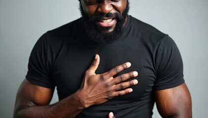 Man with beard frowns, grips chest in visible pain. Black t-shirt. A portrait showing sorrow, heartache, and emotional vulnerability. Gesture of suffering, inner conflict, and despair.