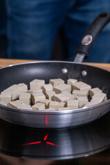 Tofu cubes sizzling in a frying pan on a stovetop, showcasing a healthy vegetarian protein option for plant-based cuisine with vibrant cooking ambiance