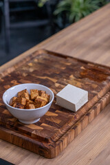 Tofu cubes in a white bowl alongside a block of fresh tofu on a wooden cutting board, showcasing healthy vegetarian protein options for plant-based cuisine