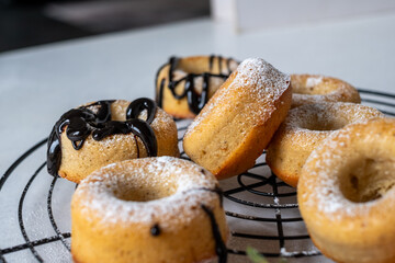 Freshly baked donuts cooling on a wire rack, dusted with powdered sugar and drizzled with chocolate, showcasing delightful pastries in a cozy kitchen setting
