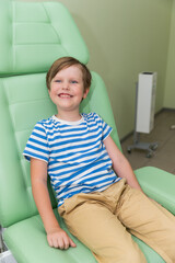 Boy sitting in otorhinolaryngologist's medical chair, smiling before medical examination