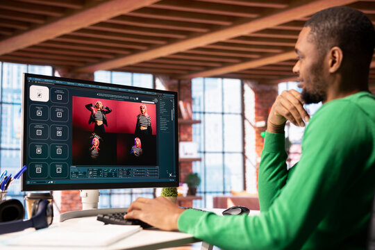 Smiling man in apartment workspace using AI software on computer display turning text prompt into photos. Upbeat african american person in home office uses text to image generative models on PC
