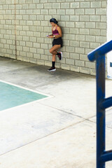 Middle aged woman checks her cellphone during a fitness routine by a gray wall, enjoying an active and connected moment that reflects modernity and self-confidence.