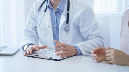 A doctor and a patient. The physician, wearing a white medical coat over a blue shirt, is filling out a medical record form during a consultation in the clinic. Medical service