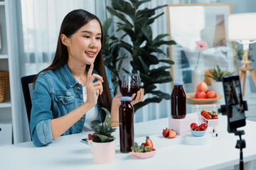 Smiling young beautiful Asian reviewing tasty mixed strawberry and cherry juice detox drinks, showing healthy product to promote for special promotion selling on social media online record. Stratagem.