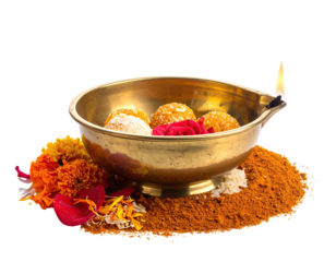 A brass bowl filled with sweet treats, a small oil lamp, and marigold flowers, resting on a bed of spices
