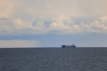 Large freight ship on the distant horizon before billowing clouds