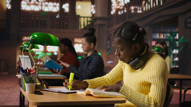 Black preteen pupil underlining key words and phrases for the learning session at the library, creating a summary to retain information easier. Focused scholar studying. Camera A.