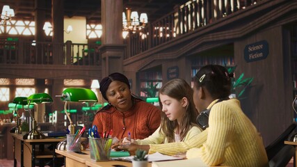 Black teacher mentoring her teen girls students with an assignment, teaching academic concepts and enhancing their knowledge through practical exercises. Private lessons at the library. Camera A.
