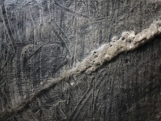 Close-up of a textured rock surface with a prominent diagonal mineral vein. Intricate natural patterns and striations highlight geological detail and earth’s natural artistry.